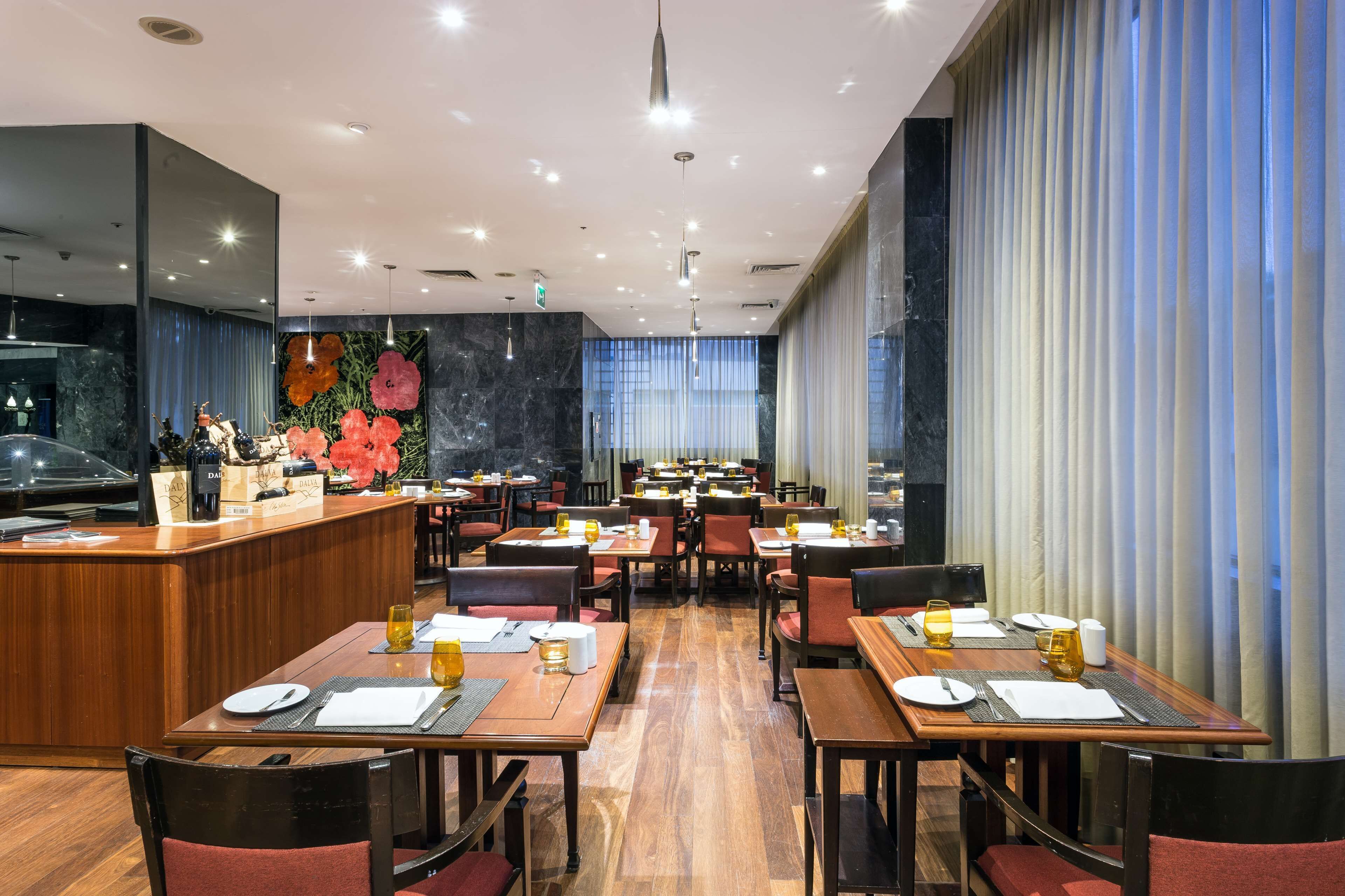 Un restaurante moderno con mesas y sillas de madera, una zona de bar y una pared decorativa con flores.