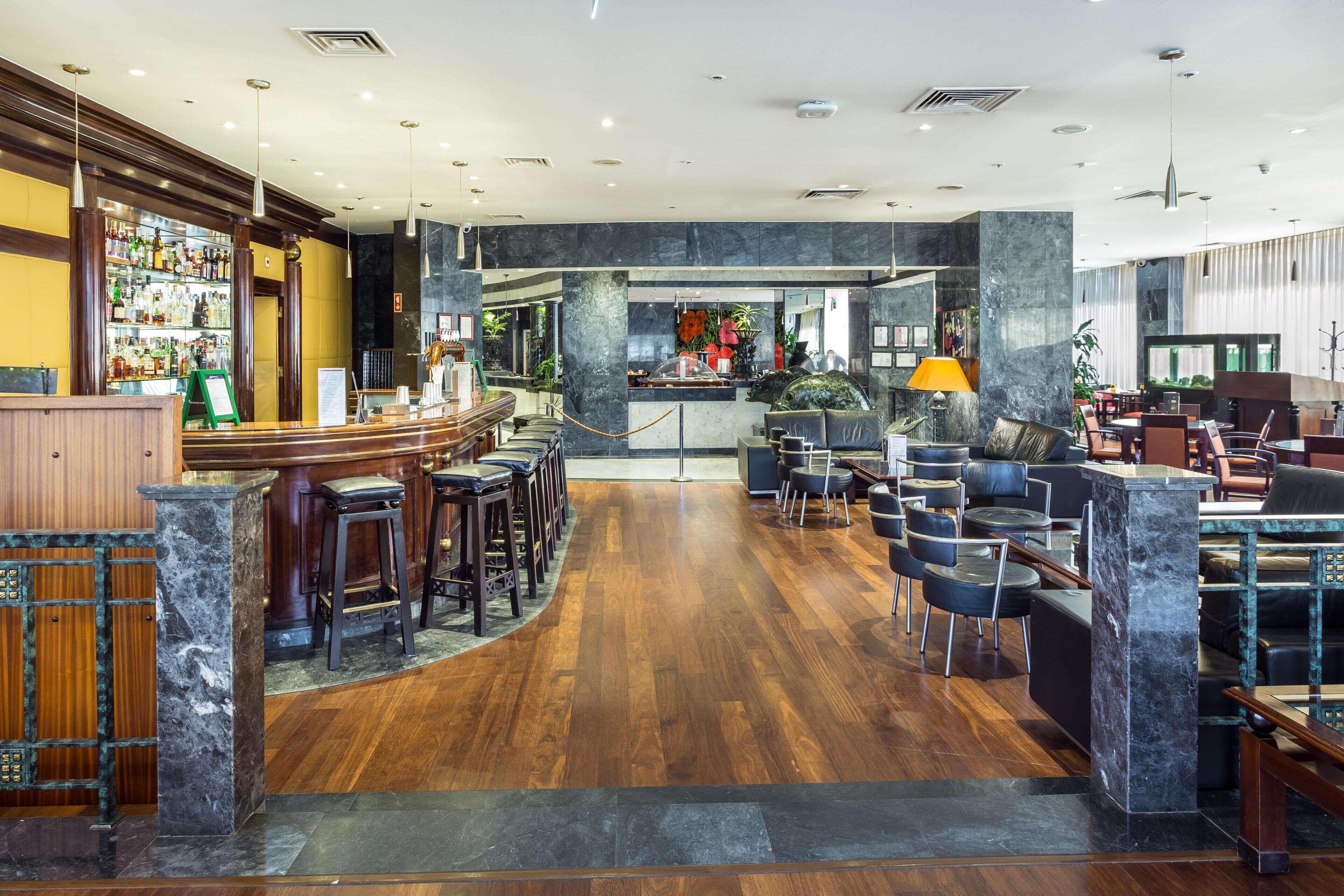 Zona de bar con taburetes, una barra y un área de asientos con mesas y sillas.