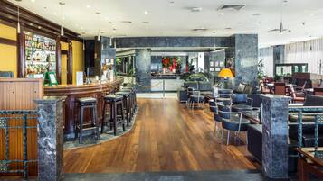Zona de bar con taburetes, una barra y un área de asientos con mesas y sillas.