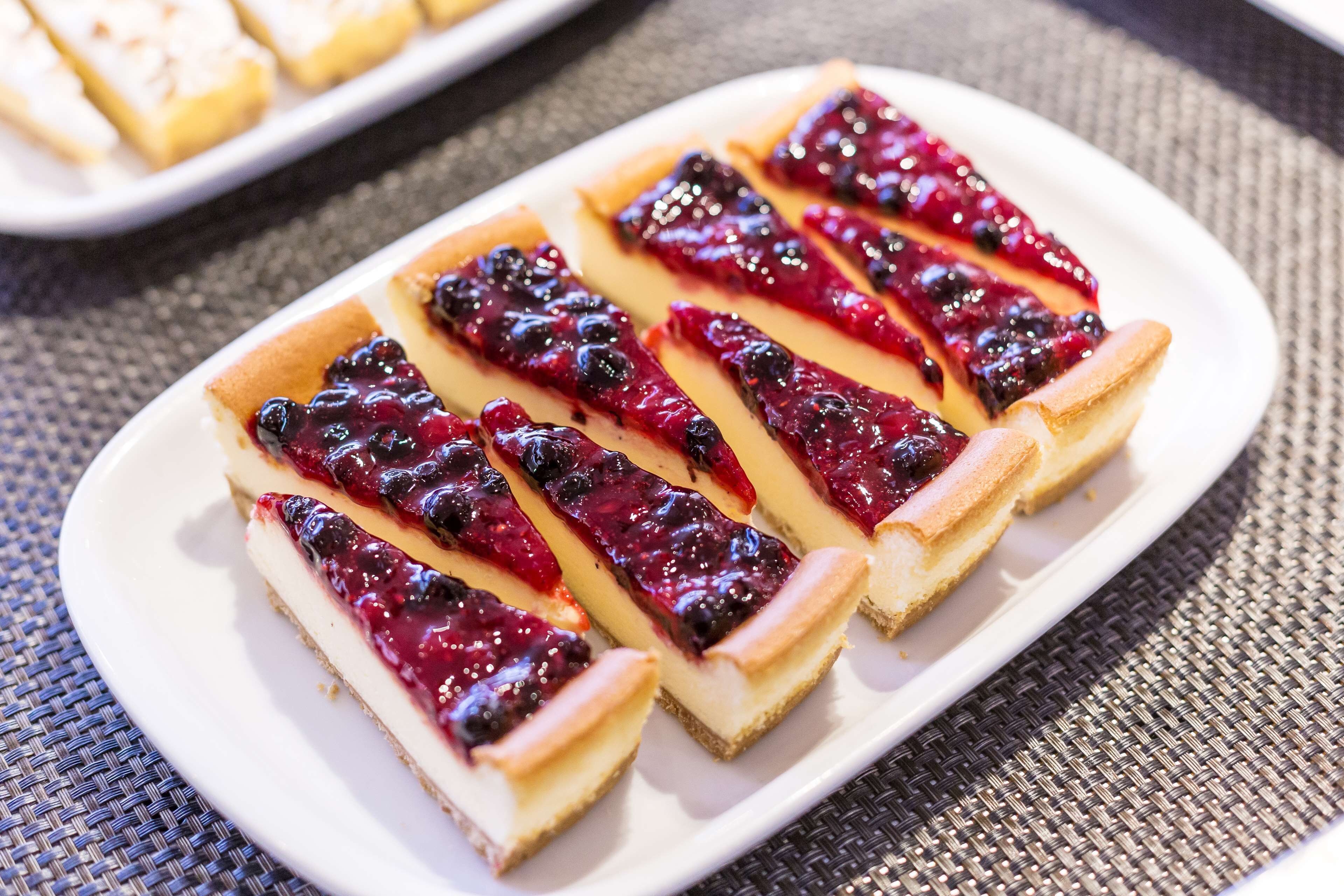 Un plato blanco con rebanadas de tarta de queso coronadas con compota de arándanos.