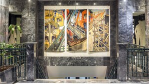 Un vestíbulo moderno con paredes de mármol, un amplio mural abstracto y una escalera.