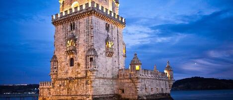 A historic stone castle with a prominent tower, situated by a calm body of water.