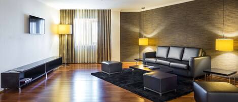 A modern living room with a leather sofa, black ottomans, a flat-screen TV, and two floor lamps.