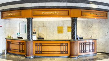 Un área de recepción con una pared de mármol y un mostrador de madera identificado con las etiquetas "CAIXA" y "PONTARIA".