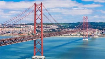 A large red bridge spanning a body of water with a cityscape in the background.
