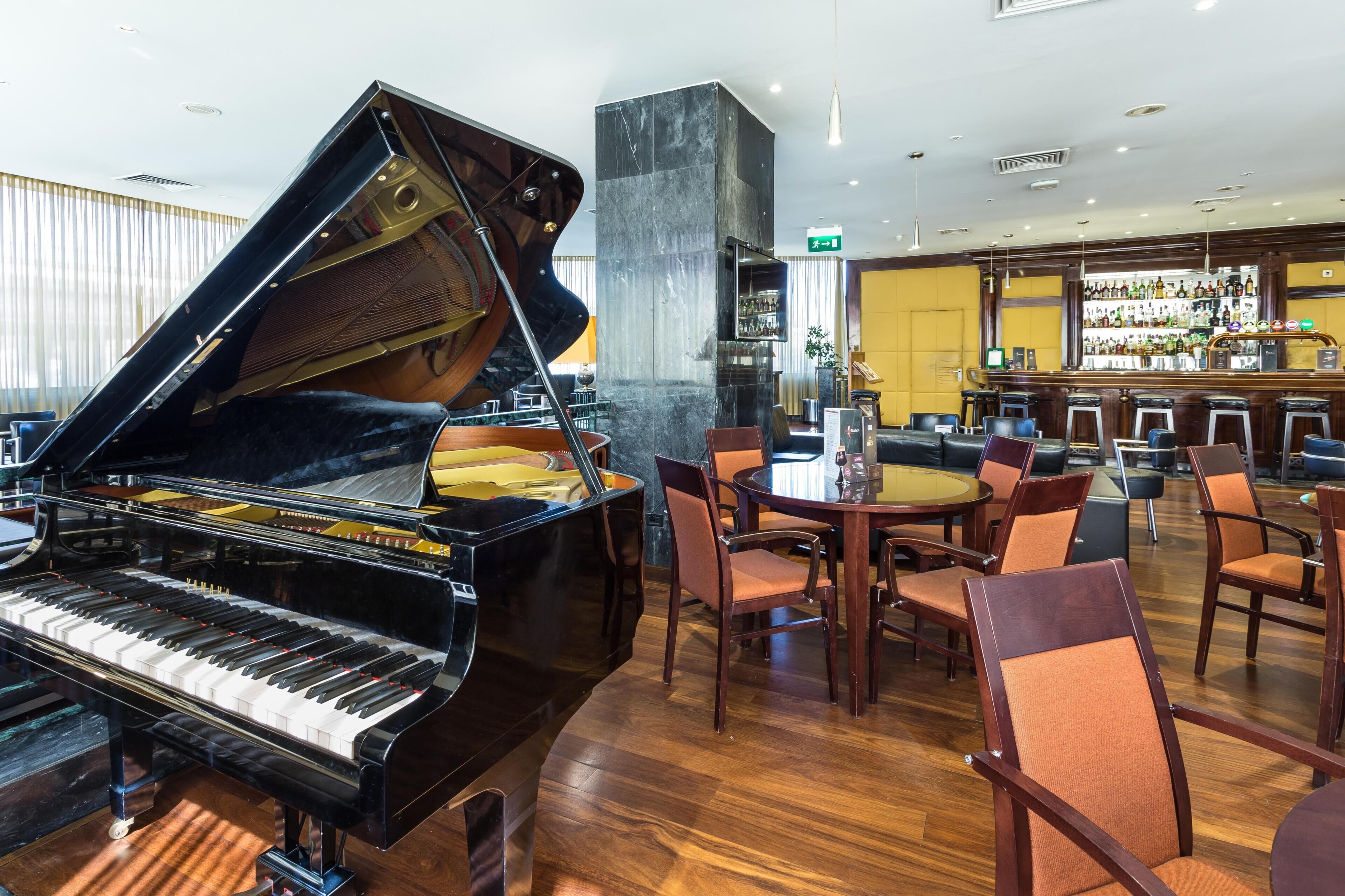 A grand piano in a spacious room with a bar and seating area.