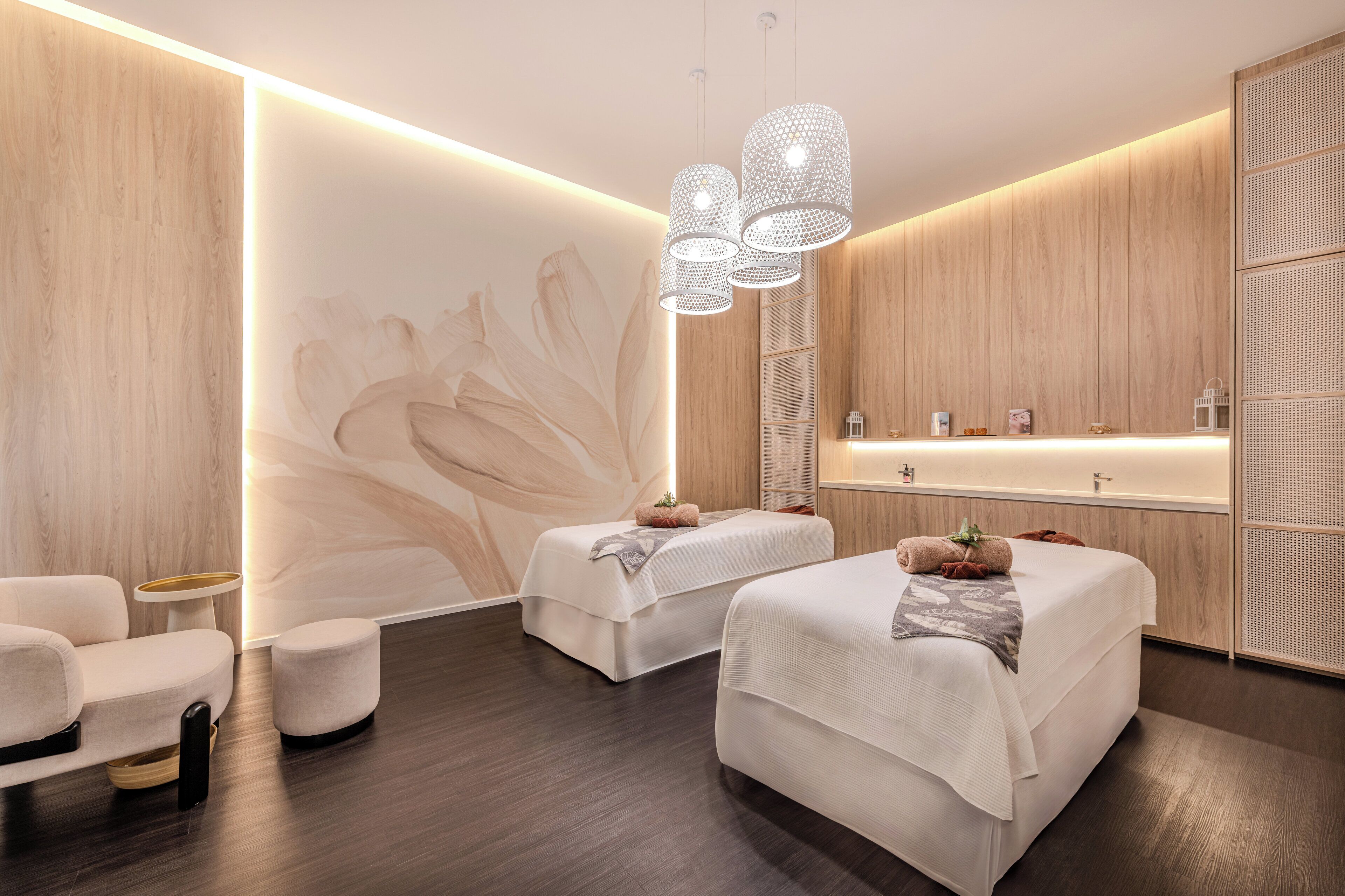 A modern spa room with two beds, a massage table, and a small seating area.