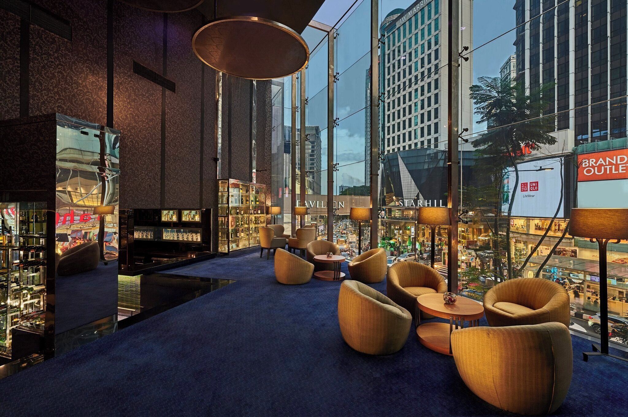 A modern lounge area with comfortable seating, a large window offering a view of the city, and a glass wall displaying a brand outlet.