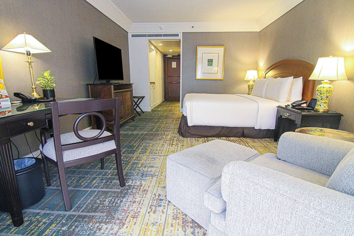 A hotel room with a bed, a desk, a chair, a television, and a lamp.