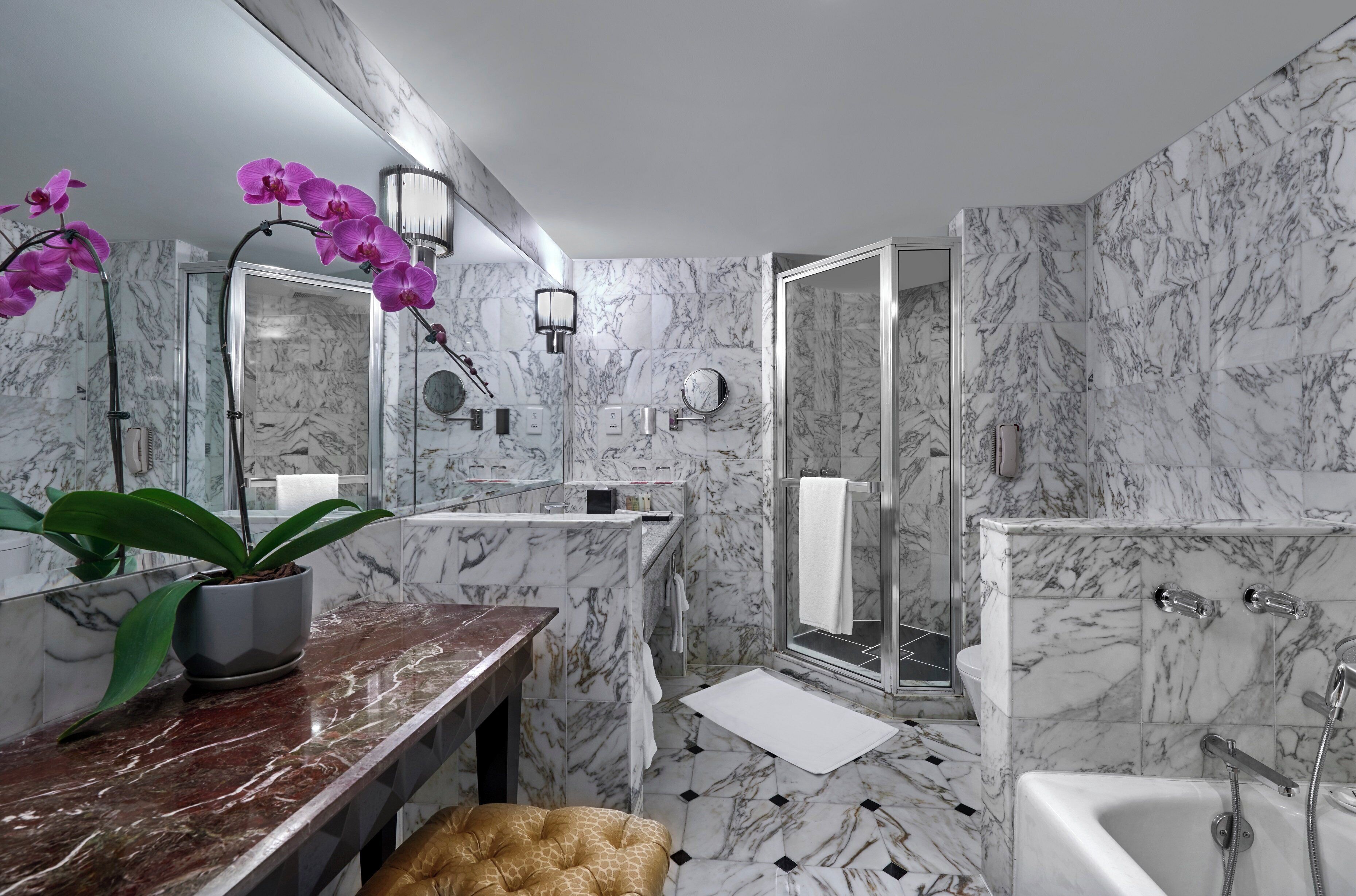 Une salle de bain moderne avec des murs en marbre, un meuble-lavabo avec un miroir, une baignoire et un espace douche.