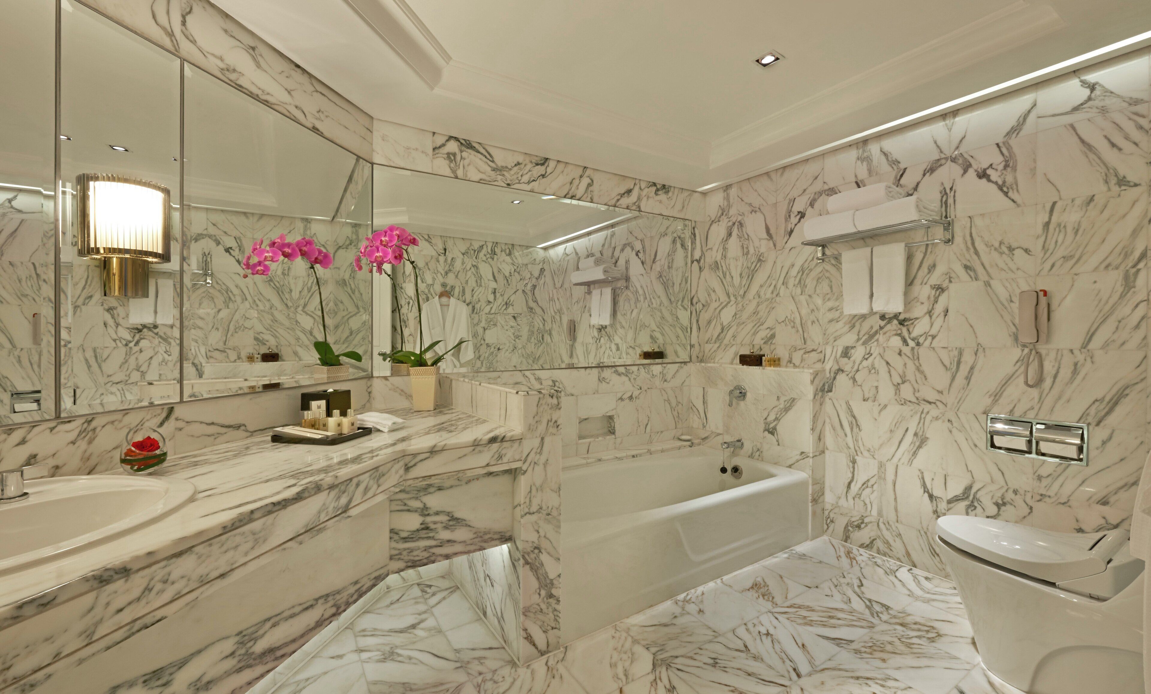 A bathroom with marble walls, a bathtub, a toilet, and a vanity with a mirror.