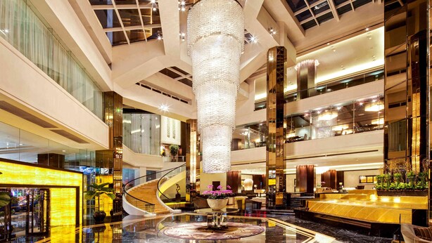 A spacious lobby with a central chandelier, a curved staircase, and a reception area.