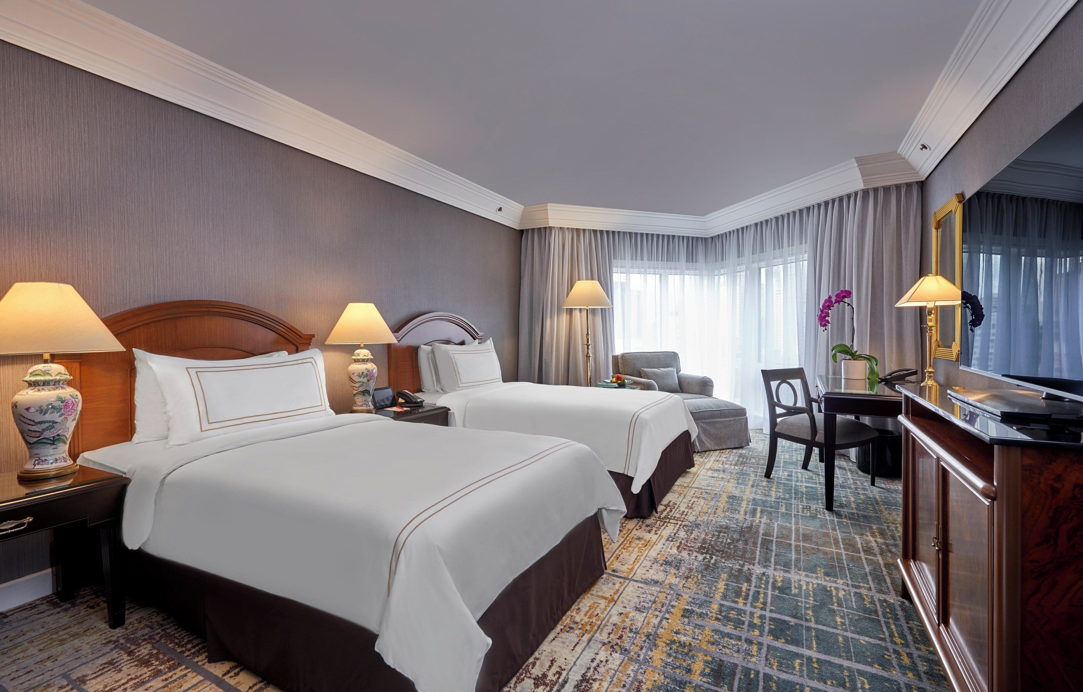 A hotel room with two beds, a desk, a chair, a TV, and a large mirror.