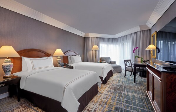 Habitación de hotel con dos camas, un escritorio, una silla, un televisor y un espejo grande.