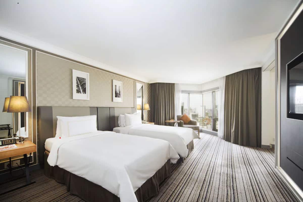 A hotel room with two beds, a large mirror, a flat-screen TV, and a city view.