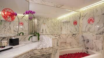 A bathroom with marble walls, a bathtub filled with rose petals, a towel rack, and a potted plant.