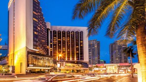 A modern hotel with a prominent tower, multiple high-rise buildings, and palm trees in the foreground.