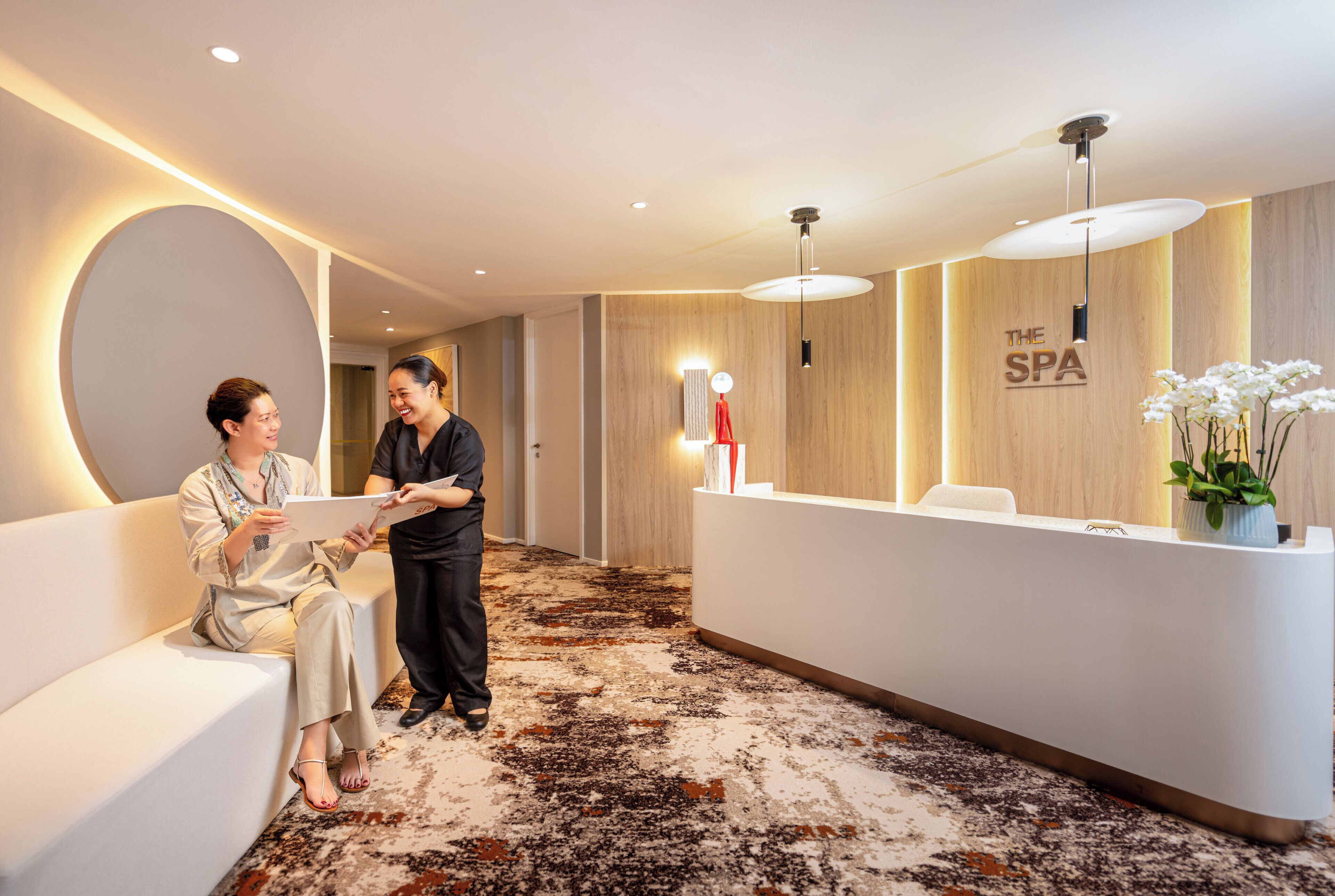 Ein Empfangsbereich mit einer weißen Rezeption, einer großen, runden Wandgestaltung und einer Rezeption mit dem Schild "THE SPA".