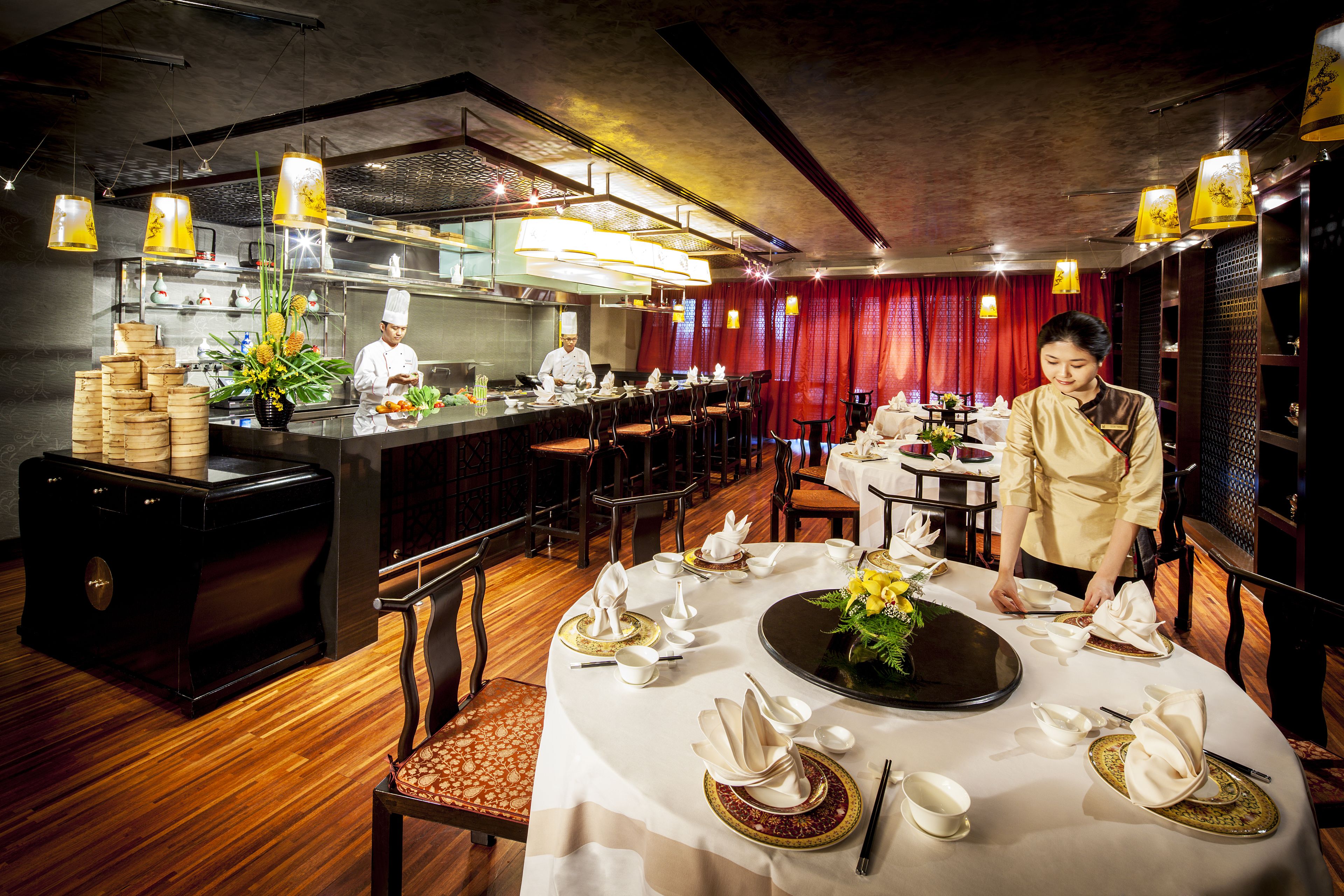 Un restaurant où un chef prépare les plats, une table dressée avec des assiettes et des couverts, et un bar avec un barman.
