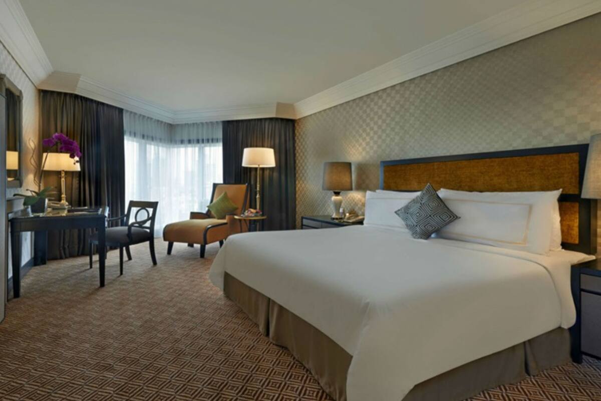 A hotel room with a large bed, a desk, a chair, and a nightstand with lamps.