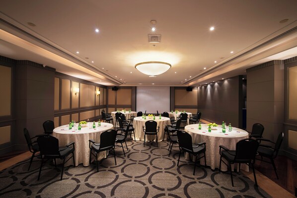 A conference room with round tables, black chairs, and a large screen at the front.