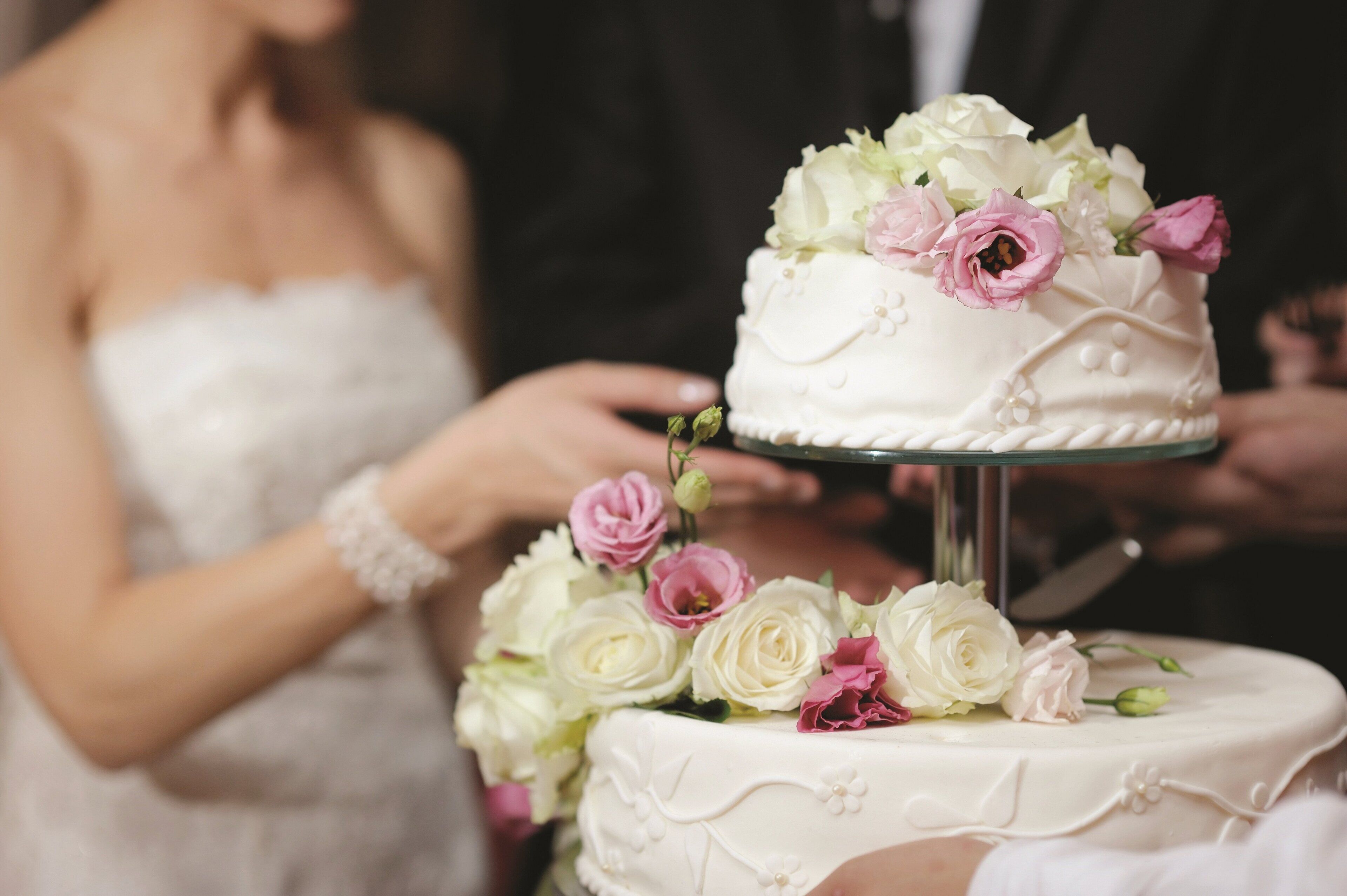 Un gâteau de mariage recouvert d’un glaçage blanc et décoré de fleurs roses et blanches, le tout présenté sur un présentoir en verre.
