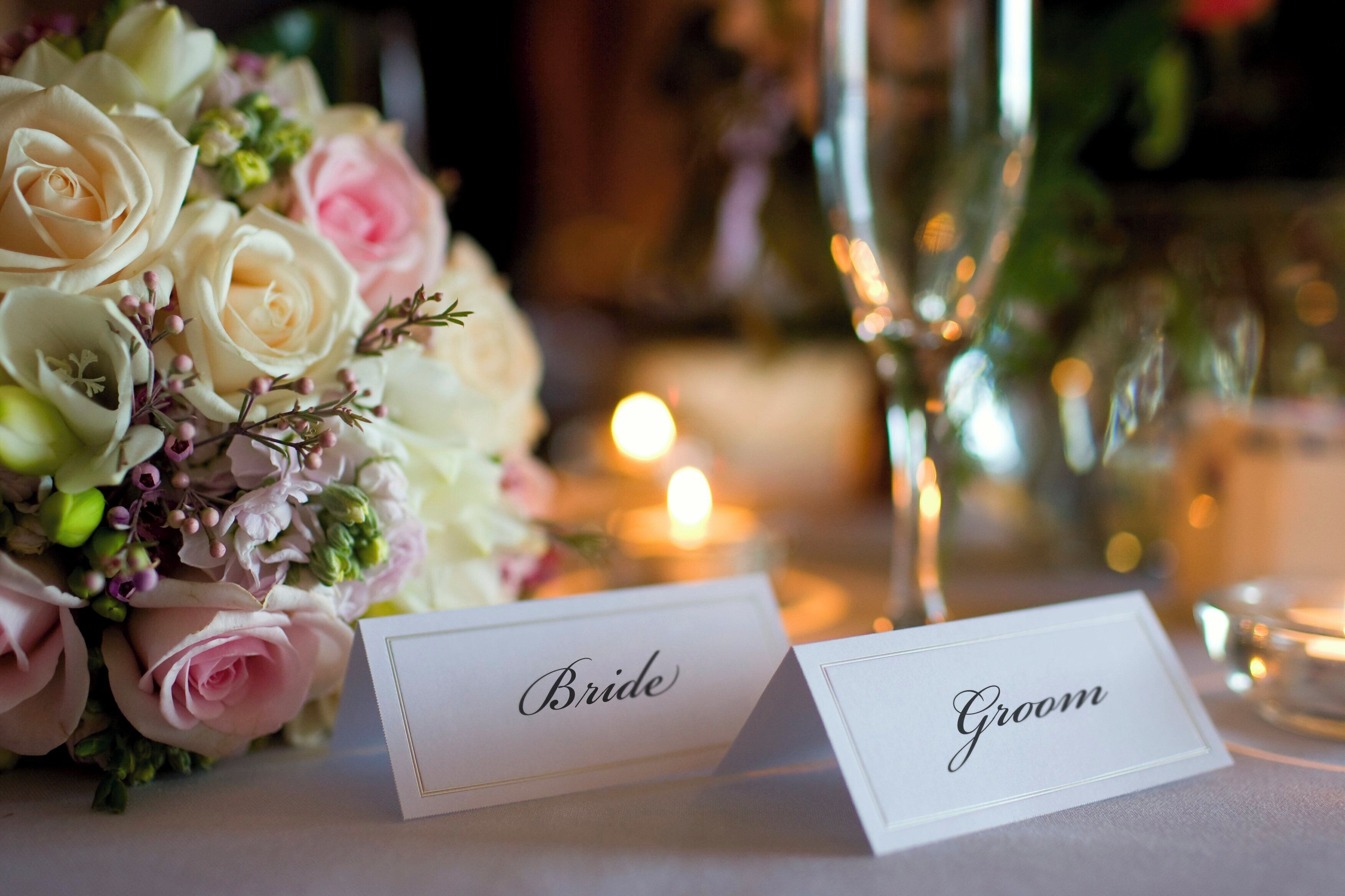 A table setting with a bouquet of roses and two name cards labeled "Bride" and "Groom".