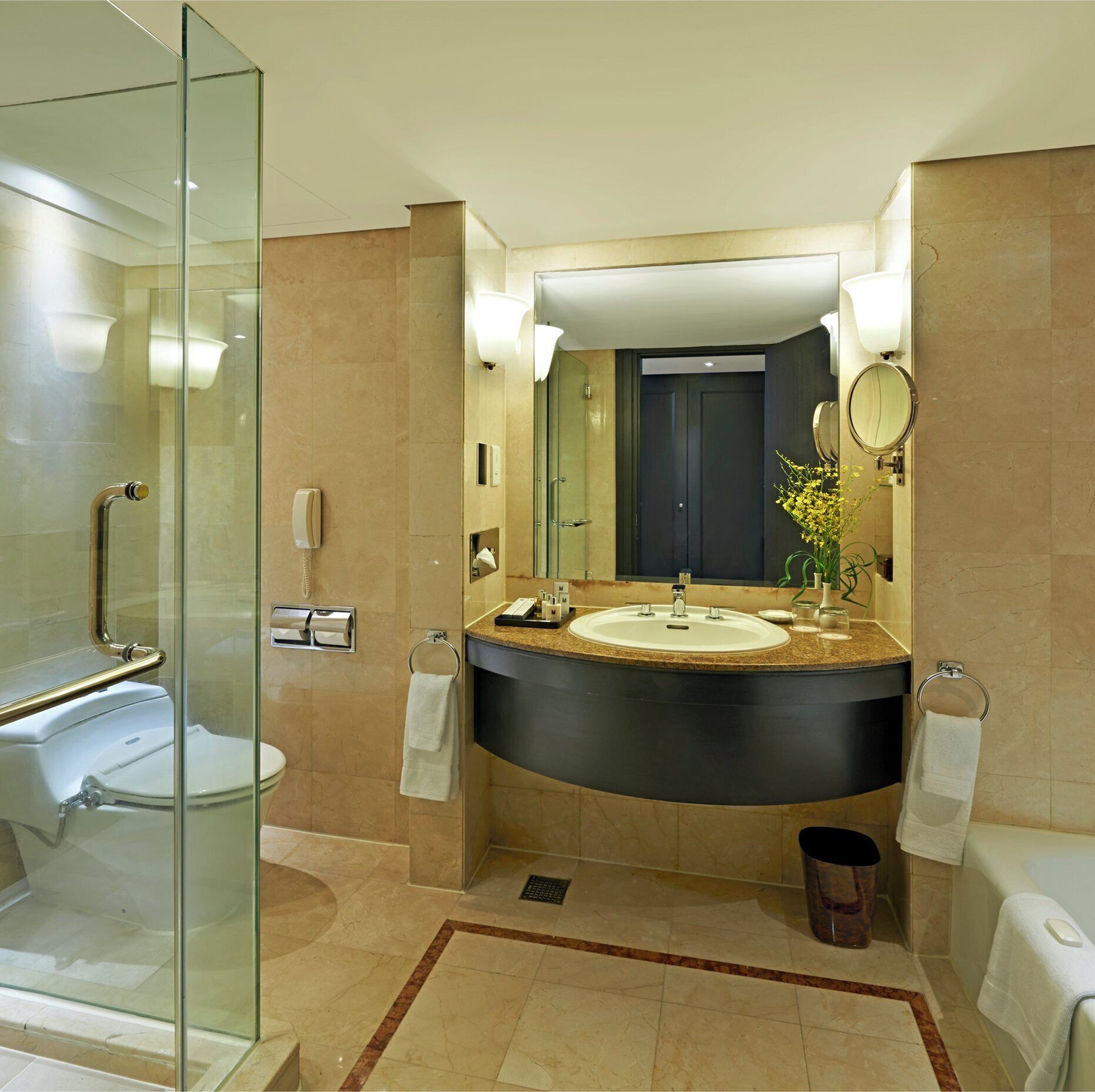 Une salle de bain moderne avec une douche à l’italienne en verre, un lavabo doté d’un plan de toilette foncé et un grand miroir au-dessus.