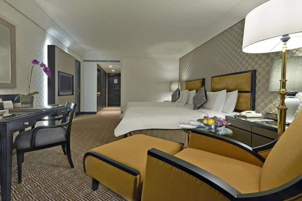 A hotel room with a bed, a desk, a chair, and a lamp.