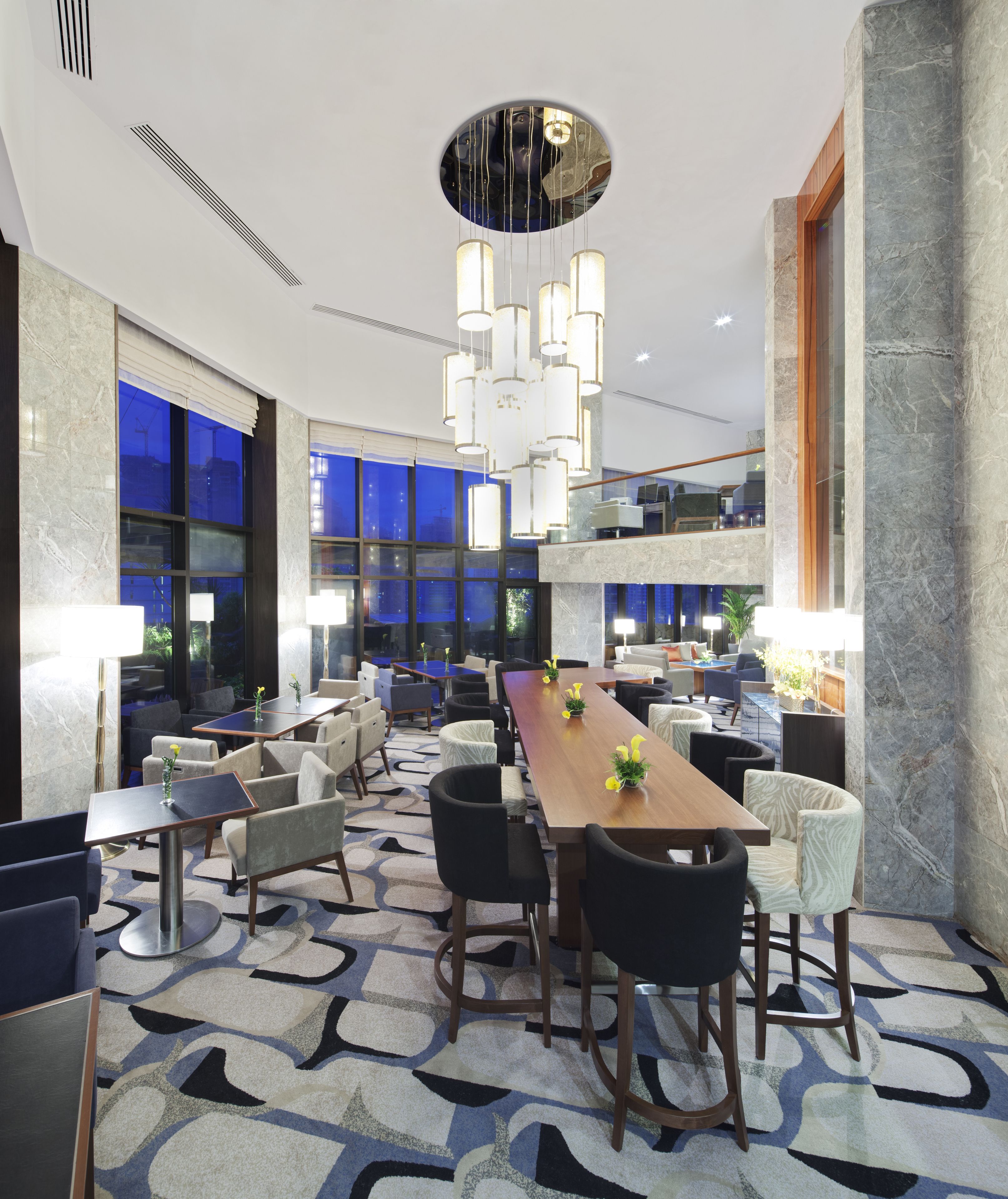 A modern hotel lobby with a long dining table, comfortable seating, and a unique ceiling design.