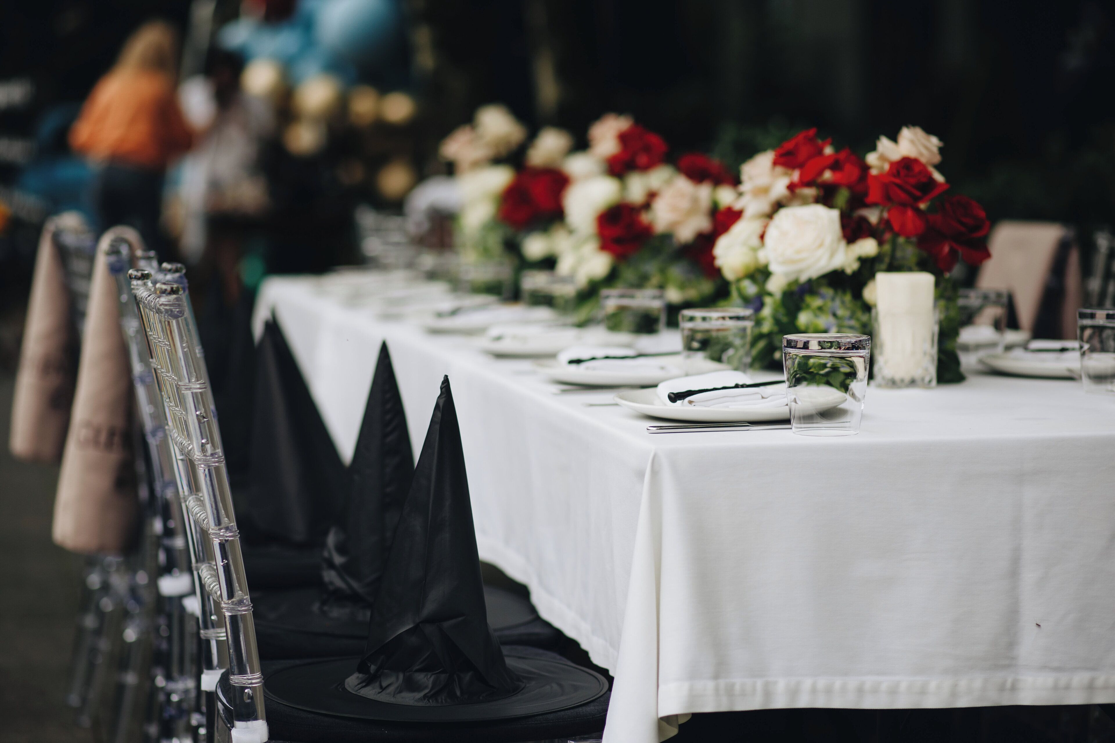 A table set for a formal event with a white tablecloth, red and white flowers, and clear glassware.