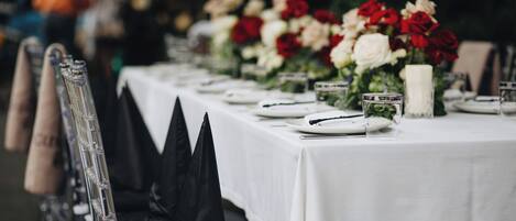 A table set for a formal event with a white tablecloth, red and white flowers, and clear glassware.