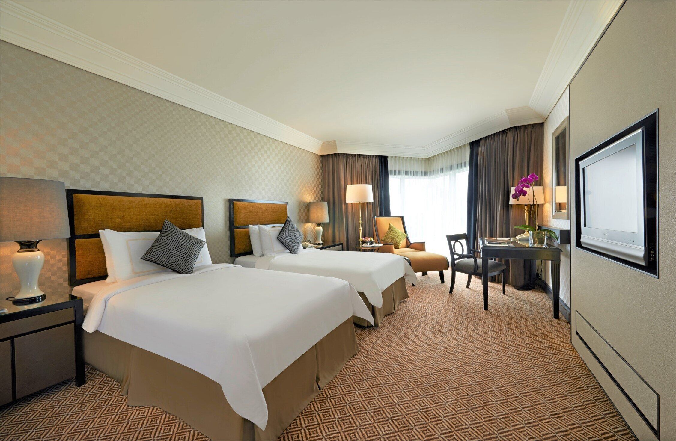 Ein Hotelzimmer mit zwei Betten, einem Schreibtisch, einem Stuhl, einem Fernseher und einem Fenster mit Vorhängen.