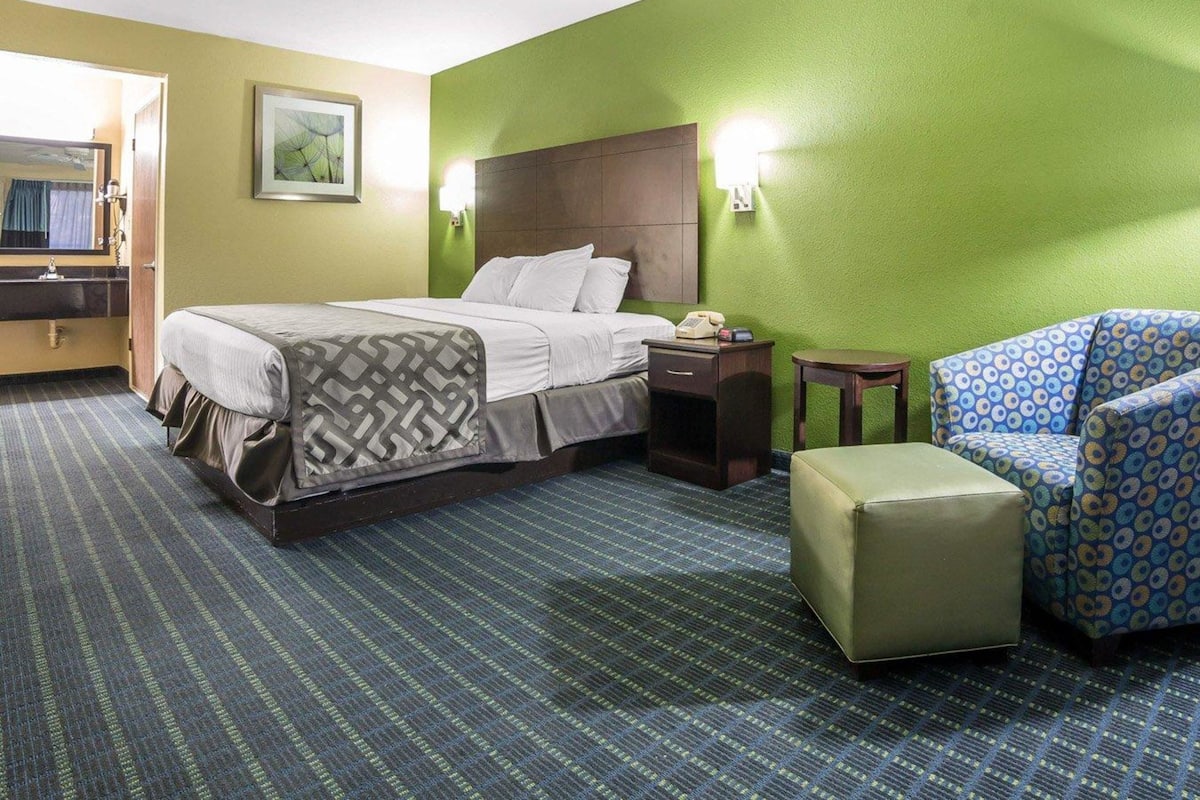 Habitación de hotel con cama, escritorio, silla, teléfono y lámpara de pared.