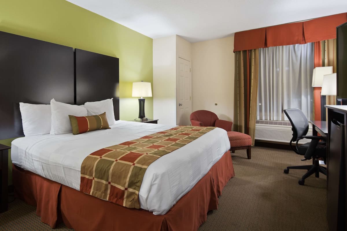 Ein Hotelzimmer mit einem großen Bett, einem Schreibtisch, einem Stuhl und einem fenster mit Vorhängen.