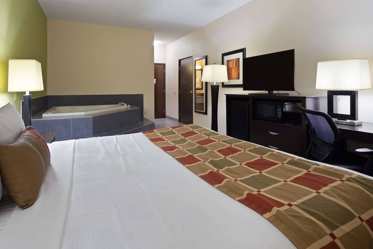 Ein Hotelzimmer mit einem großen Bett, einem Schreibtisch, einem Sessel, einem Fernseher, einer Mikrowelle und einem Badezimmer mit einer Badewanne.