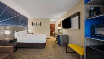 Una habitación de hotel con una cama grande, un escritorio, una silla, un banco, un televisor y un microondas.