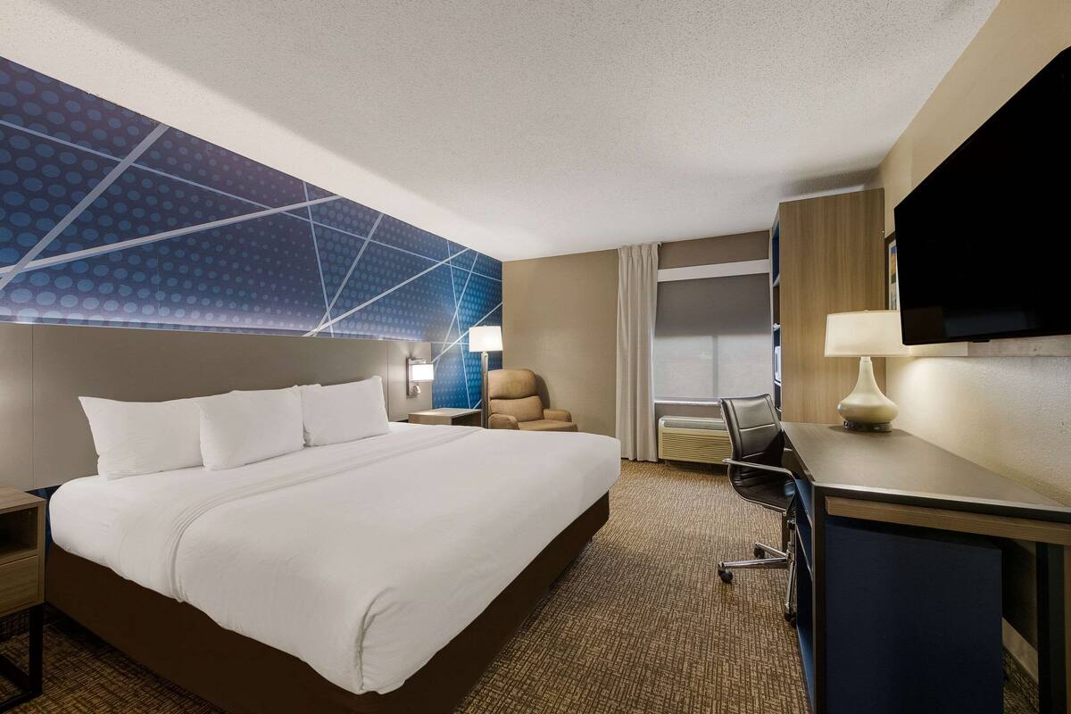Habitación de hotel con una cama grande, un escritorio con computadora, una televisión y una pared con diseño geométrico.