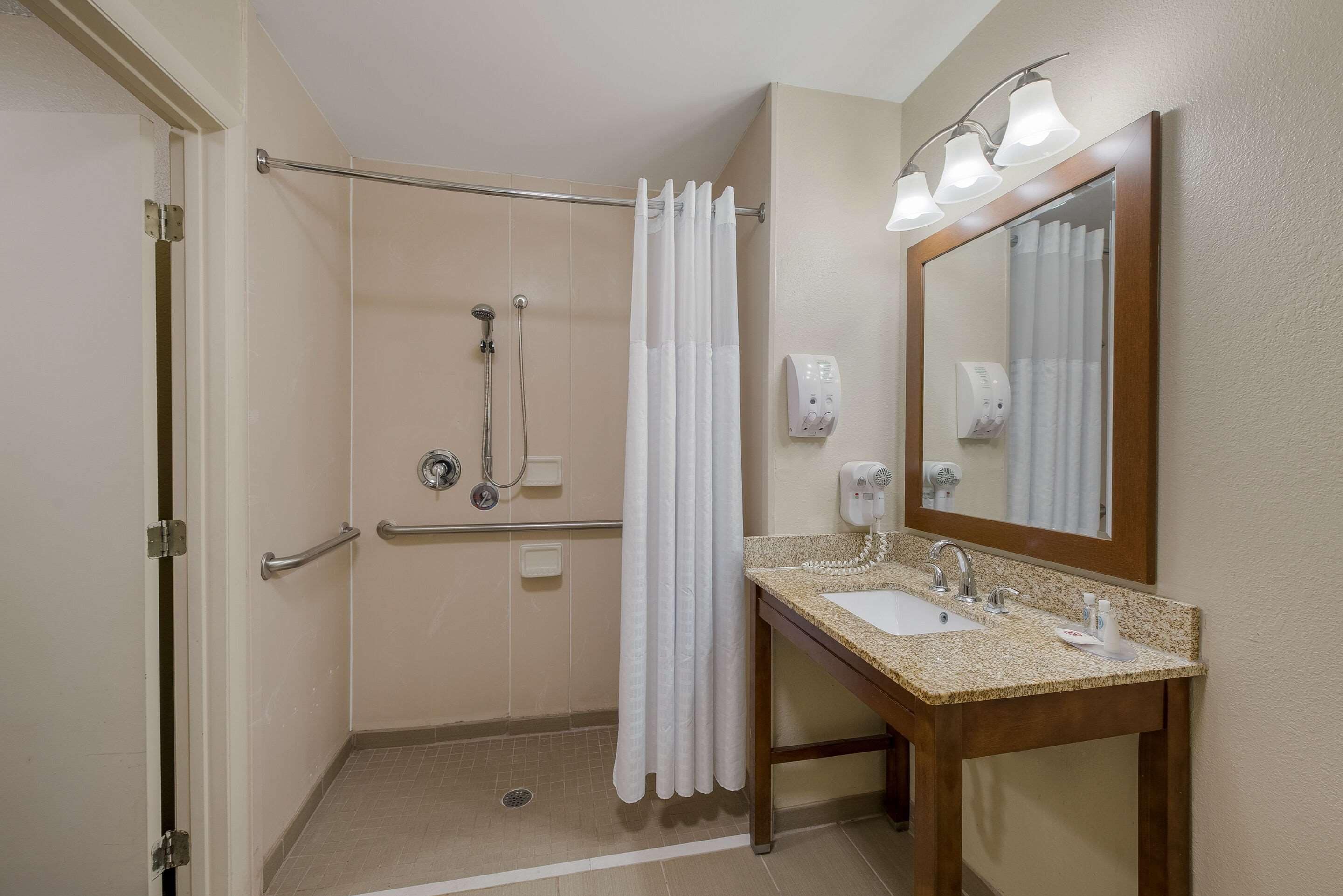 A bathroom with a shower, a sink, a mirror, and a hand dryer.