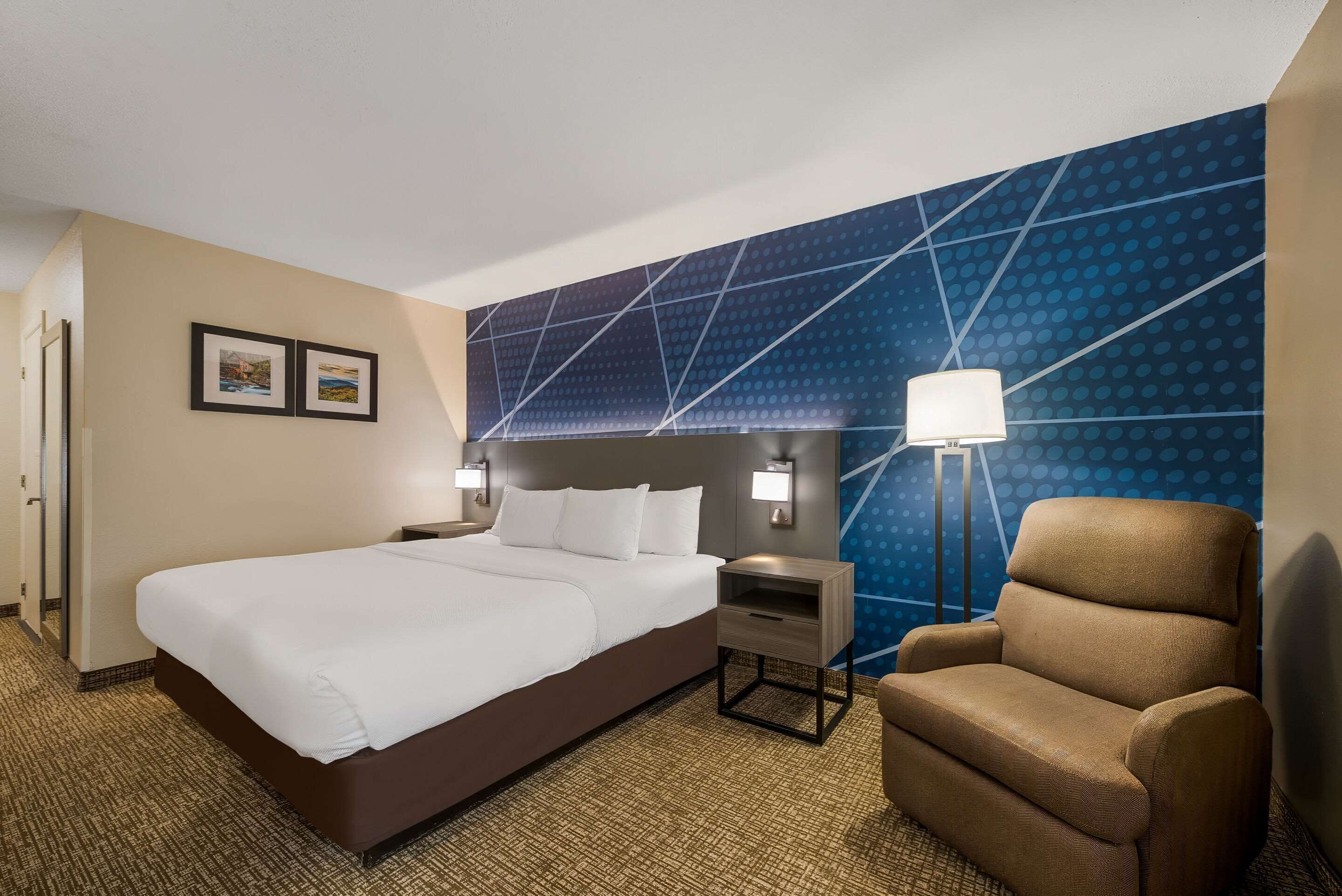 A hotel room with a large bed, a nightstand, a chair, and a wall with a geometric pattern.