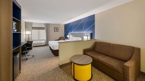 A hotel room with a bed, a sofa, a desk with a chair, a small table, and a trash bin. - Comfort Inn Fayetteville I-95 (Fayetteville)