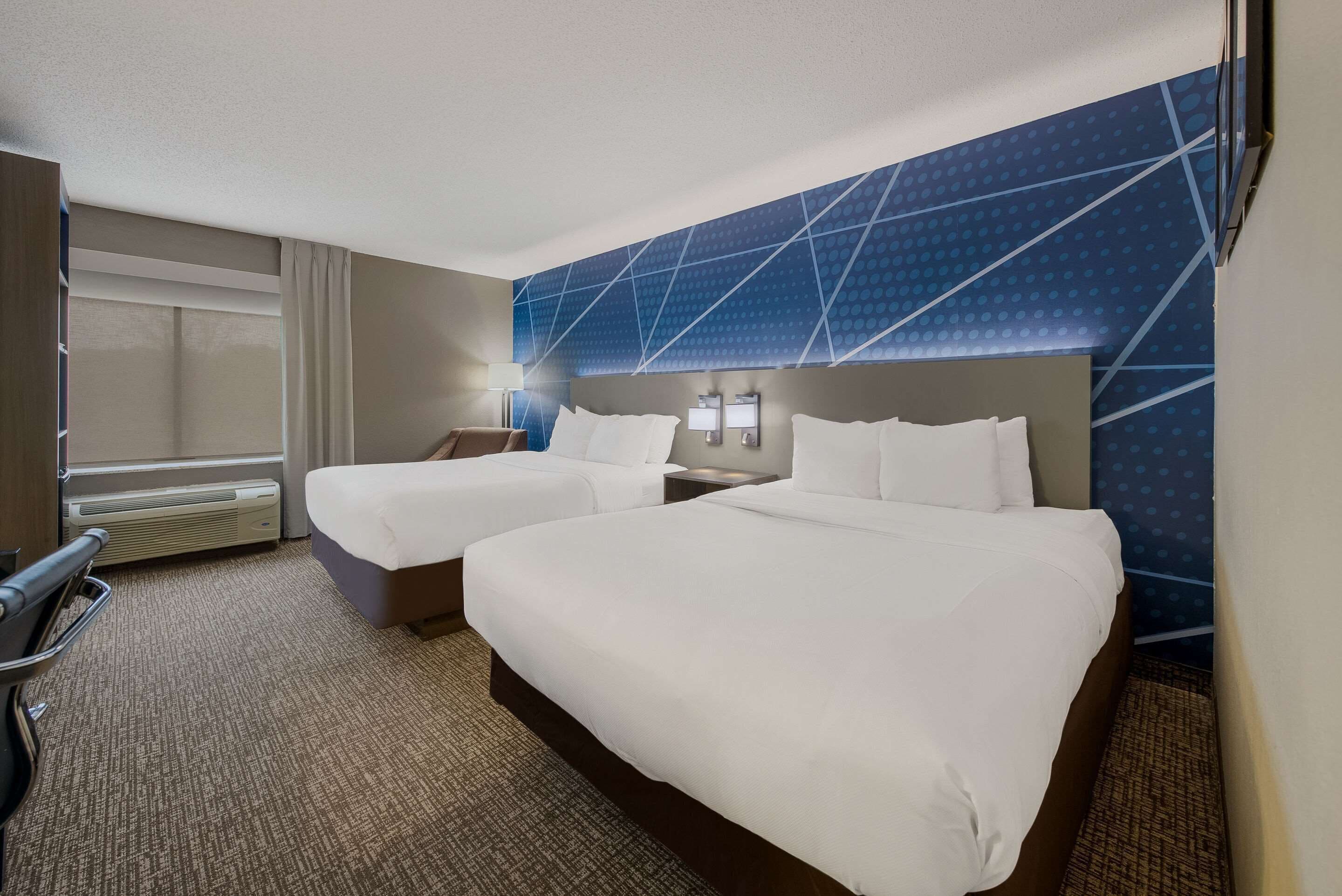 A hotel room with two beds, a desk, a chair, and a TV.