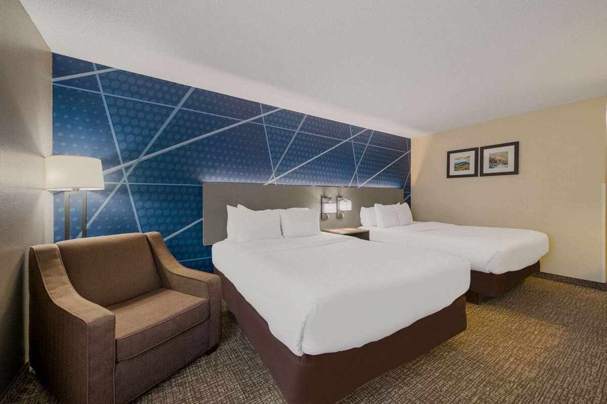 Habitación de hotel con dos camas, un sofá, una pared con diseño geométrico y dos cuadros enmarcados.