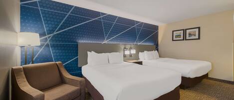 Une chambre d’hôtel avec deux lits, un canapé, un mur orné d’un motif géométrique et deux tableaux encadrés accrochés au mur.