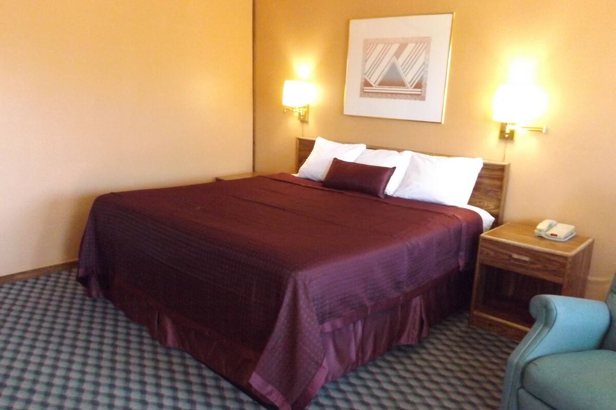 A hotel room with a large bed, two bedside lamps, a nightstand with a phone, and a patterned carpet.