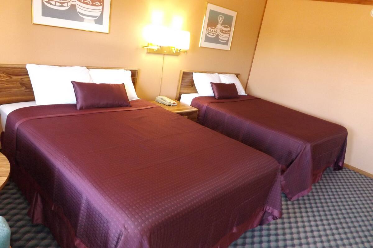 A hotel room with two beds, each with a purple bedspread, a wooden headboard, a bedside table with a lamp, and a telephone.