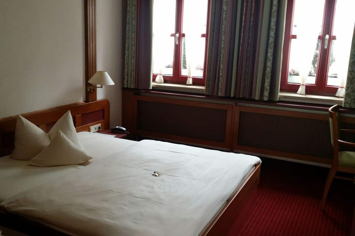 Une chambre d’hôtel avec un lit, un bureau, une chaise et une fenêtre avec des rideaux.