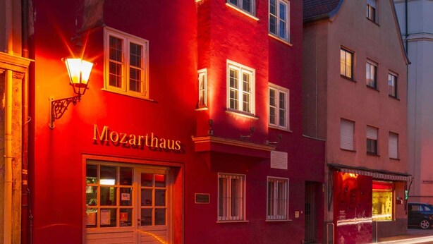 Un edificio rojo con el nombre 'Mozarthaus' en la planta baja, de estilo arquitectónico europeo tradicional, con numerosas ventanas y una entrada destacada.