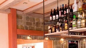 Una zona de bar con taburetes, una pared de piedra y estantes llenos de botellas.