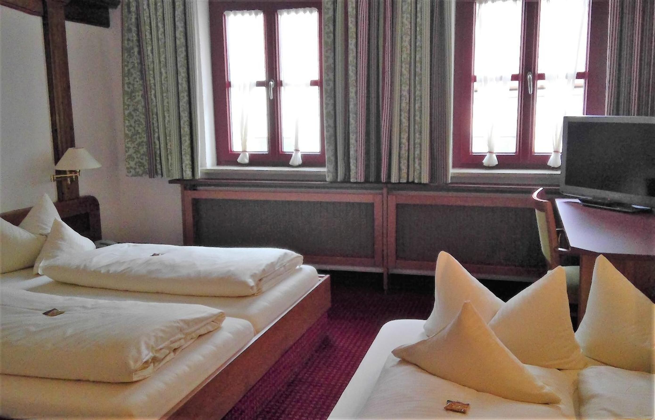 A hotel room with two beds, a television, and a window with curtains.